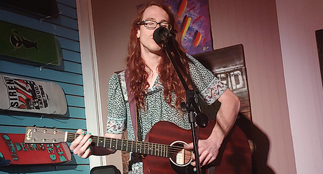 nails painted green blouse martin acoustic skateboard decks on wall behind singing microphone black spandex pants